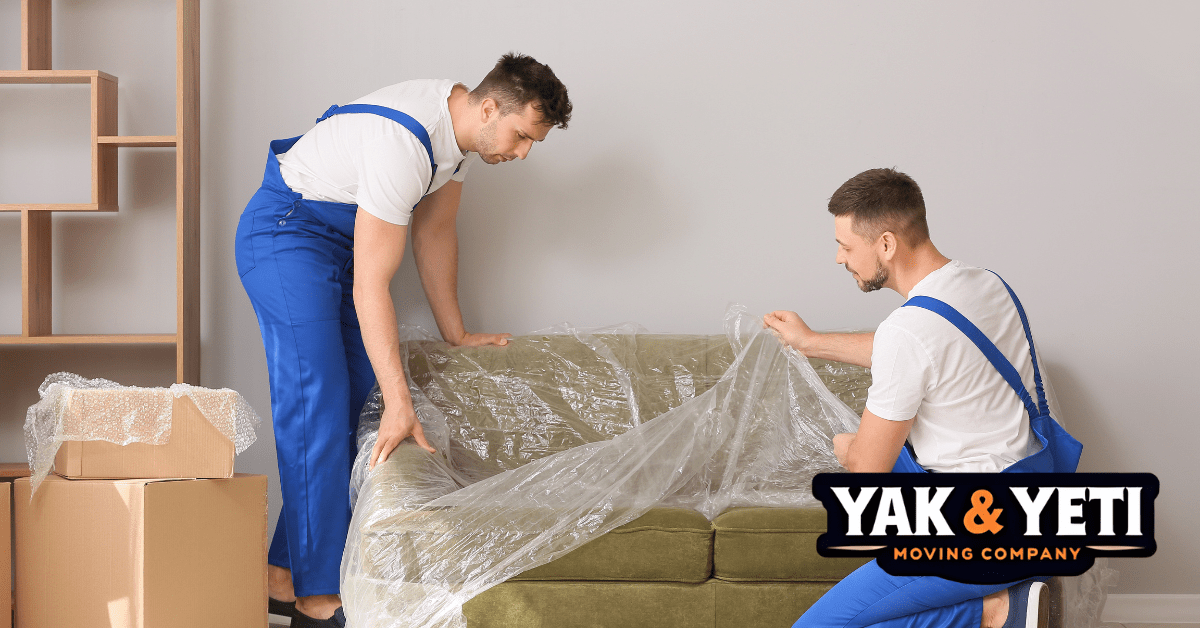 men in blue overalls holding plastic over a couch